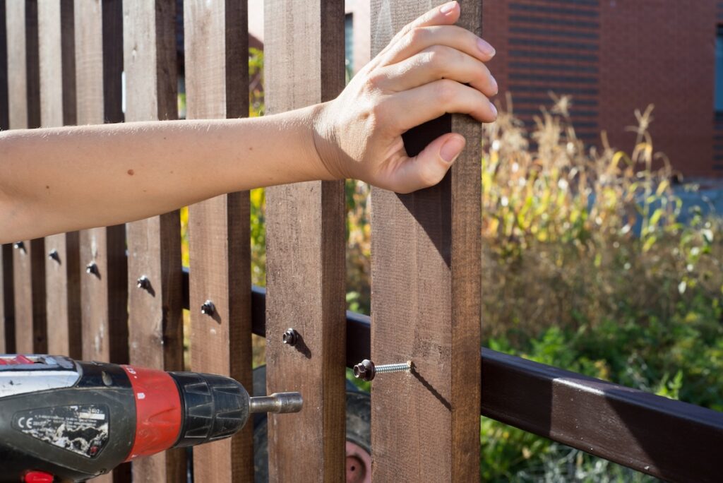someone using a drill to fix a wooden fence