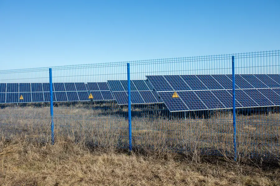 Security mesh fence with electrical warning signs surrounding a large outdoor solar panel farm