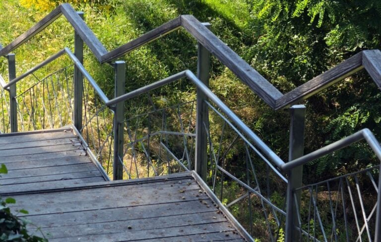 High angle view of a wooden park staircase with a geometric zigzag metal handrail descending a hillside
