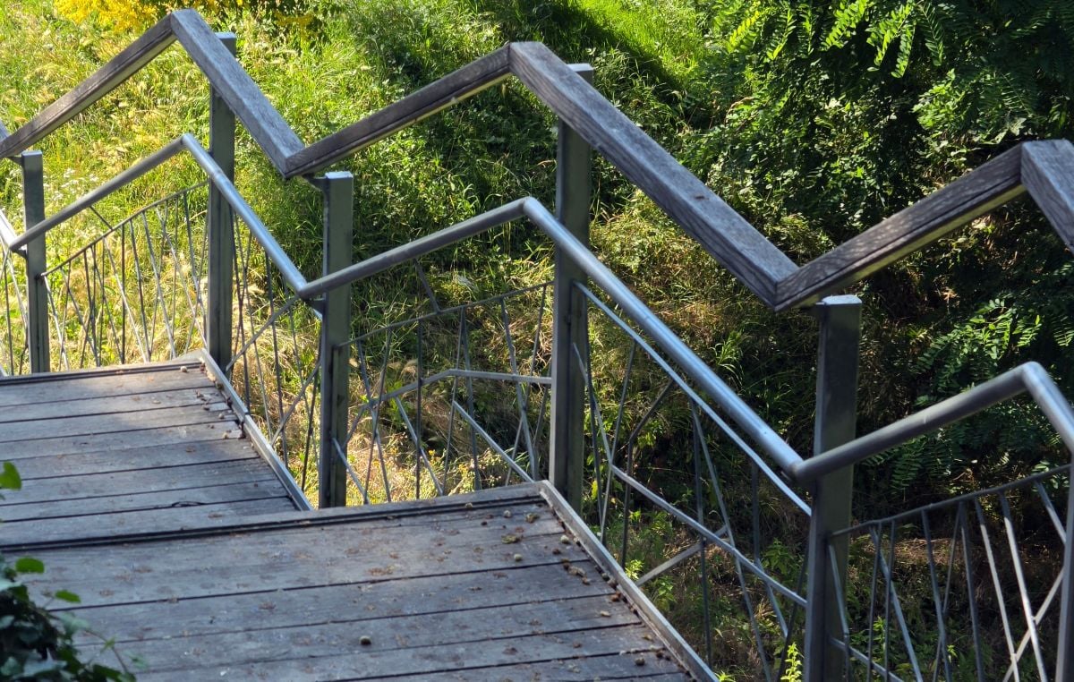 High angle view of a wooden park staircase with a geometric zigzag metal handrail descending a hillside