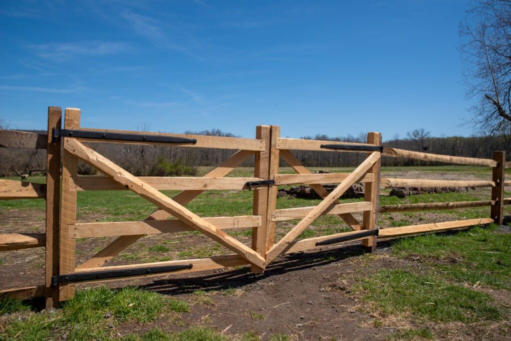 A brand new split rail wooden fence gate in a sunny pasture

