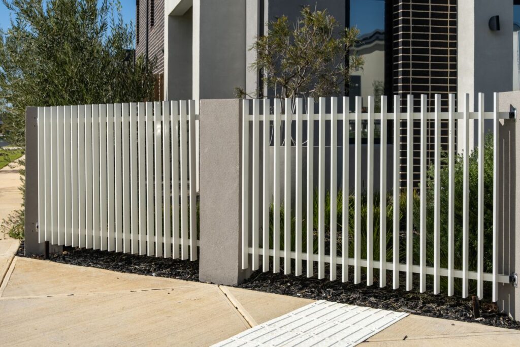 A modern white aluminium picket fence with rendered concrete posts fronts a contemporary new home