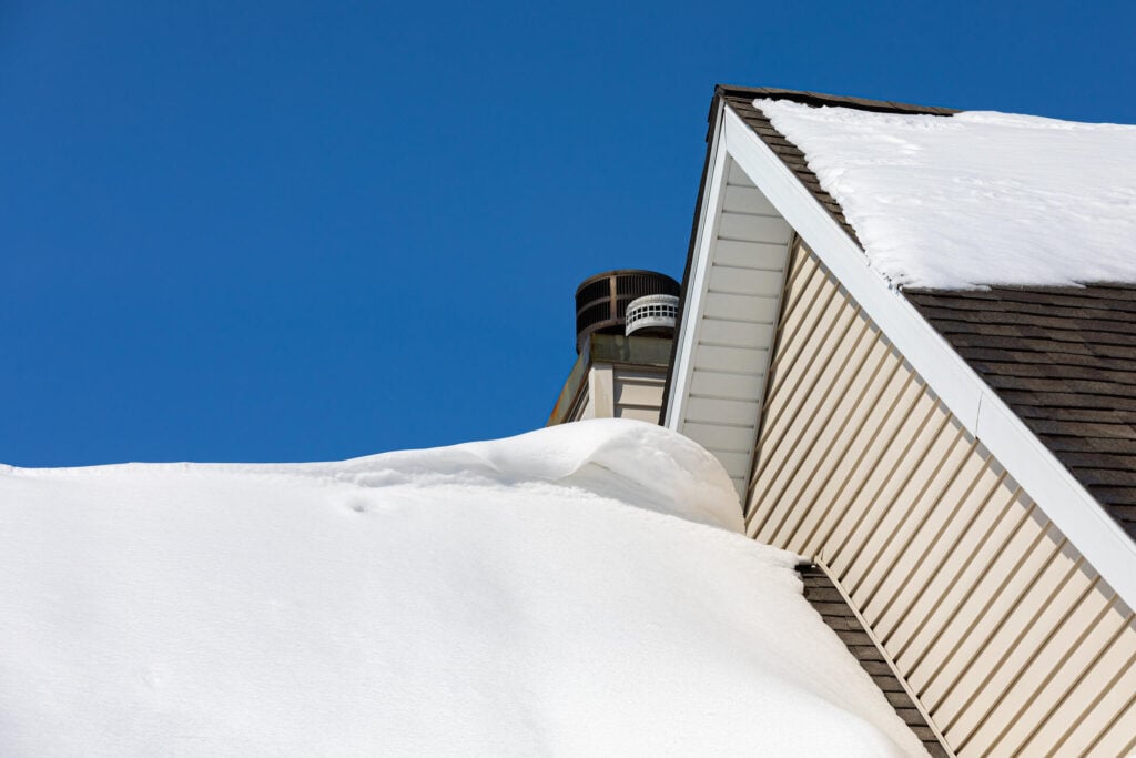 Snow drift on roof of house after winter storm. Roof damage, snow removal