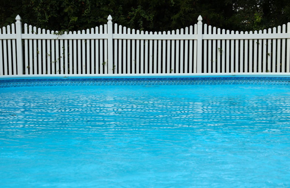 Swimming pool and white vinyl fence in front of trees