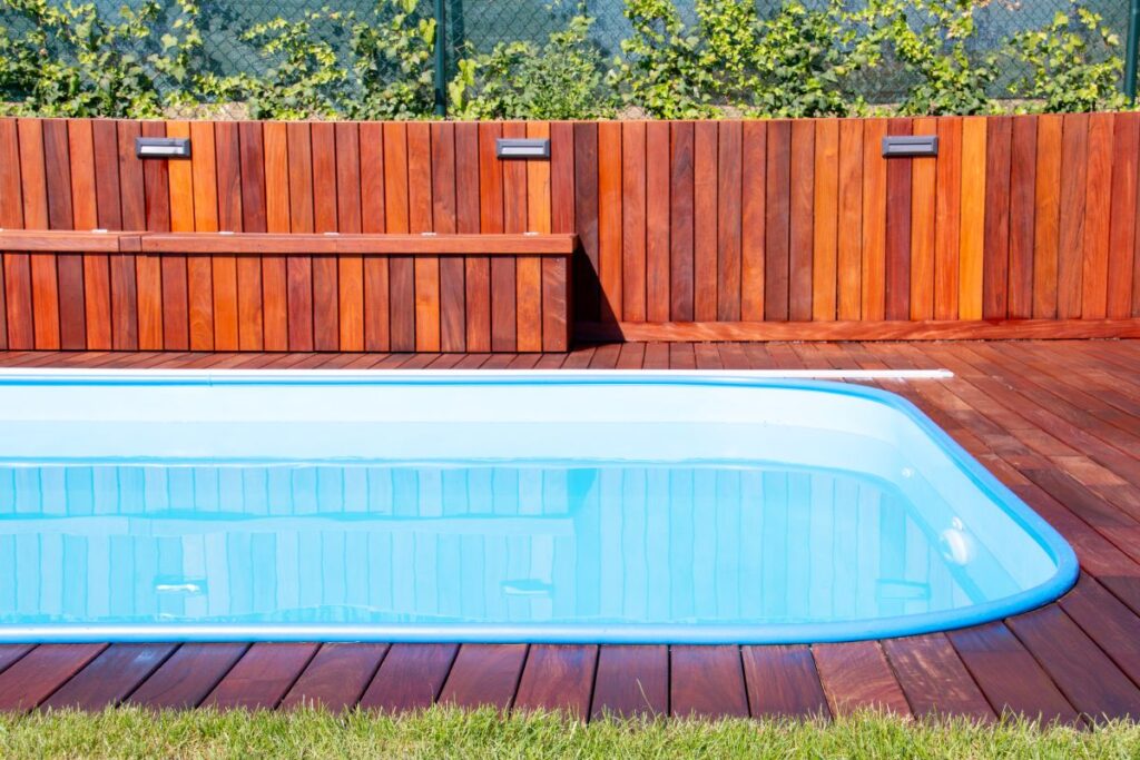 Swimming pool with wood floor and deck fence with greenery
