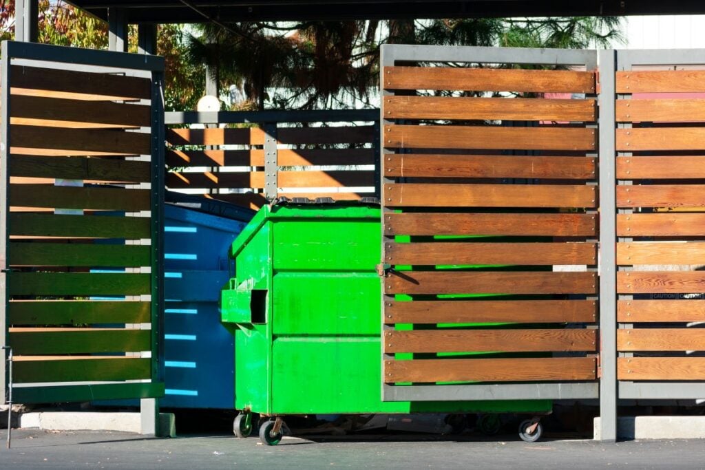 Two waste management blue and green garbage containers dumpsters in garbage enclosure used for commercial and residential garbage