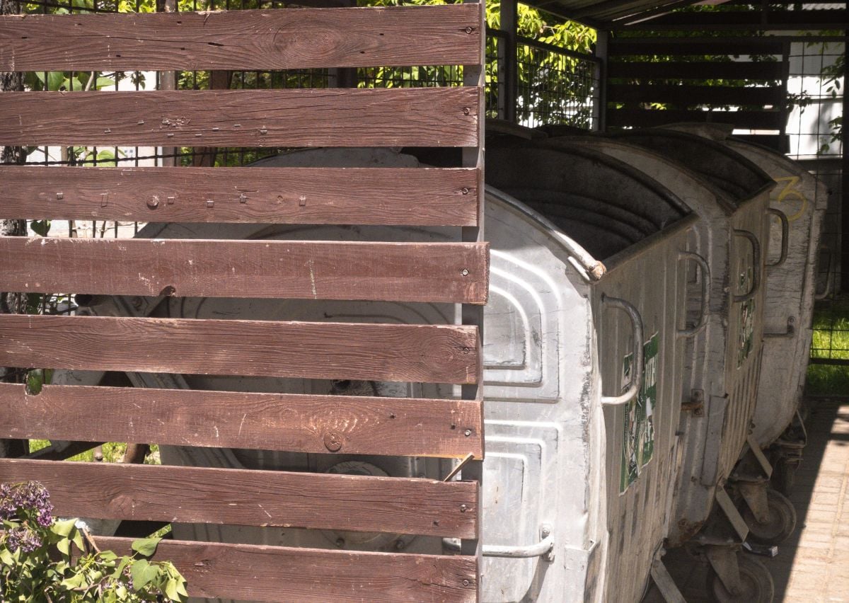 Waste container shelter with wooden partition and metal dumpsters