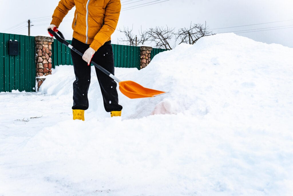 Woman removes snow from her yard using plastic shovel in cold winter